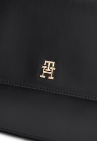 Černá kožená kabelka s jemným prošitím a malým zlatavým proplétaným logem "TH" na přední klopě.
