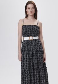 Zwarte maxi-jurk met bloemenpatroon, tiered ontwerp, verstelbare spaghetti-bandjes en een brede witte riem met een vierkante gesp.