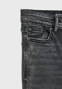 Černé džíny z denimu s klasickým designem pěti kapes, se stříbrnými detaily a jemným vyblednutím látky. Detailní pohled na oblast pasu.