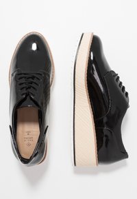 Chaussures à lacets en cuir verni noir avec une semelle plateforme beige à texture croisillonnée et un bord en caoutchouc blanc. Texture lisse, design classique.