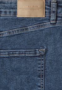 Partie de la poche arrière d'un jean en denim bleu avec une étiquette en cuir marron sur laquelle est inscrit "Street One Denim All Time Favourite."