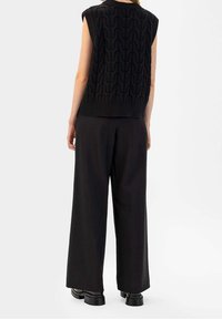 Haut sans manches en maille noire avec un motif ondulé texturé, associé à un pantalon noir à jambes larges. Finition lisse et coupe décontractée.