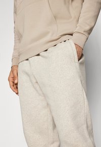 Beige hoodie met een subtiele textuur, voorzien van een kangoeroezak. Gecombineerd met lichtbeige sweatpants, beide in een zachte, elastische stof.