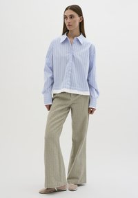 Camicia a righe blu chiaro e bianca con colletto e maniche morbide, abbinata a pantaloni beige larghi e testurizzati con motivi verticali.
