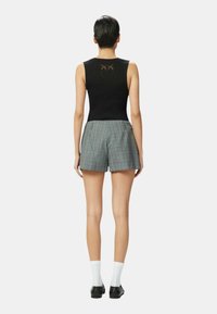 Camiseta sin mangas de rayas negras con un diseño cosido en la parte posterior, combinada con pantalones cortos a cuadros en azul, gris y crema, usados con calcetines blancos y zapatos negros.