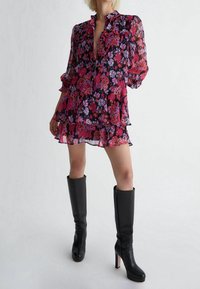 Abito mini a strati floreale in tonalità di rosa e viola su uno sfondo nero. Tessuto trasparente con bottoni, abbinato a stivali neri con tacco al ginocchio.