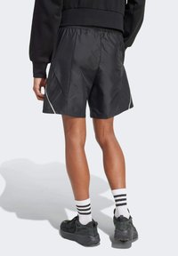 Sorte atletiske shorts med en glat overflade, elasticitet i taljen og kontrasterende hvide sømme. Krydret med mørke sneakers og stribede sokker.