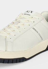 Бял маратонка Armani Exchange с бели връзки, черно лого с текст отстрани и на езица, и черна текстурирана подметка.