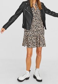 Zwarte leren motorjack, een jurk met panterprint en franjes aan de onderkant, en witte veterschoenen met dikke zwarte zolen.