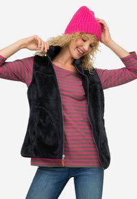 Czarna polarowa kamizelka z zamkiem z przodu, zestawiona z szaro-różową, w paski koszulą z długim rękawem oraz jasnoróżowym dzianinowym czapką. Casualowy, ciepły strój.