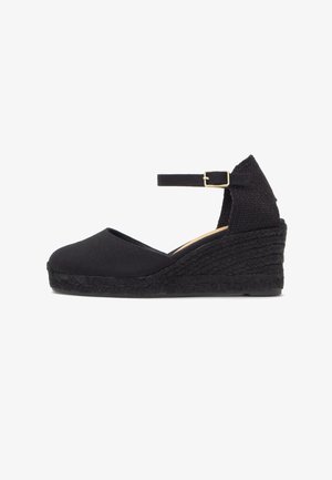 Espadrille noire à talon compensé avec bride de cheville et boucle, talon plateforme tissé texturé, bout fermé, et dessus en tissu.
