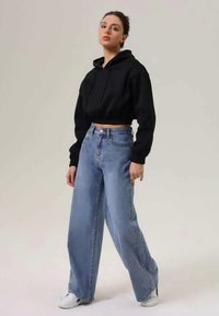 Crop hoodie preto, jeans de perna larga azul claro, ténis brancos, textura suave, ajuste casual, sem padrões visíveis. Fundo minimalista.