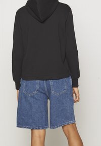 Svart huvtröja med ribbade muddar, ihop med blå denimshorts med rak ben och två bakfickor.