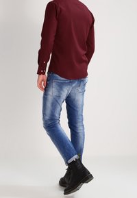 Camicia bordeaux a maniche lunghe con polsini a bottoni, abbinata a jeans in denim chiaro e stivali neri con lacci. Presenta una vestibilità dritta e uno stile casual.