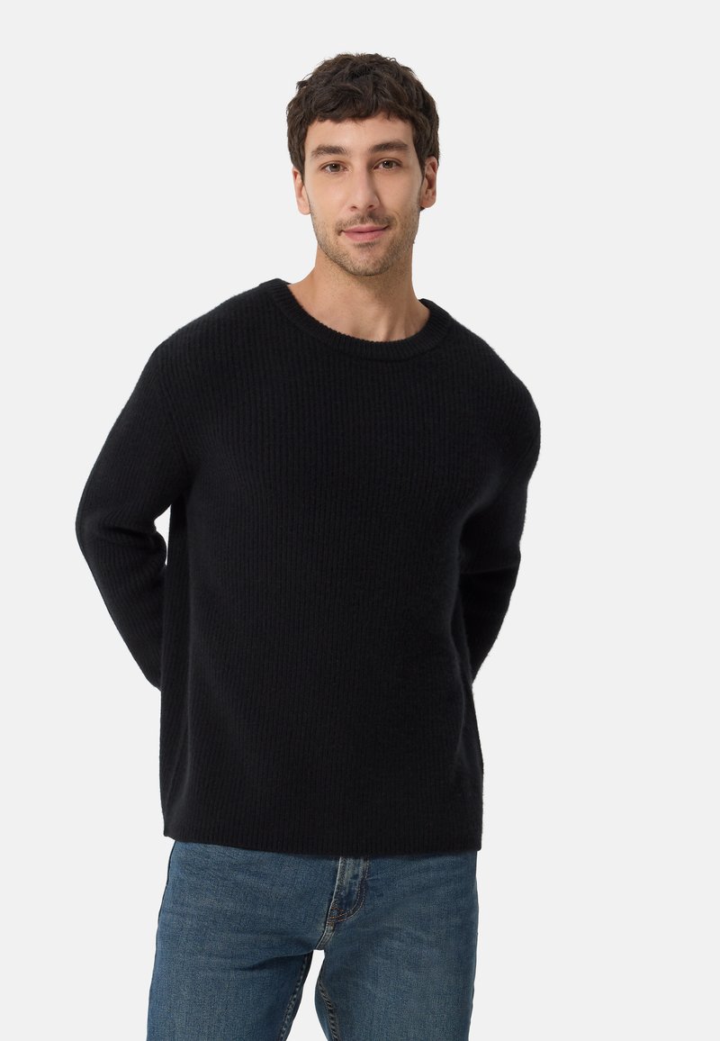 Svart ribbad tröja med rund halsringning och avslappnad passform. Mjuk textur, långa ärmar, kombinerad med blå jeans.