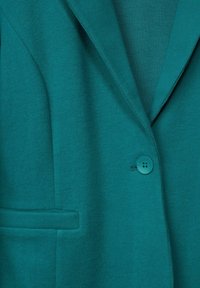 Teal jacka med notchal som har en knappstängning och en framficka; mjuk textur med en slät yta.