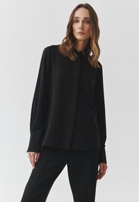 Black button-up shirt with long sleeves, featuring a textured surface with small, dotted embellishments. Smooth fabric with a relaxed fit.