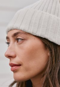 Bela rebrasta pletena kapa z navpičnimi črtami. Mehka tekstura. Približen posnetek profila osebe, ki prikazuje podrobnosti kože in las.