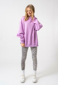 Túlméretes lila pulóver, kerek nyakkal és leengedett vállakkal, amelyhez testhezálló szürke leggings társul, fekete leopárdmintás dizájnnal.
