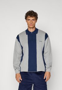 Langermet polo i grått og marineblått med halv-zip krage. Har vertikale striper og en liten brodert logo på brystet.