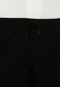 Μαύρο παντελόνι στην μέση με θηλιές για ζώνη και δεμένο μαύρο κορδόνι, σε συνδυασμό με λευκό τοπ που είναι μπαίνει μέσα.