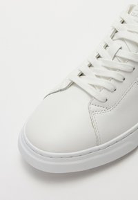 Sneaker bianco in pelle caratterizzato da punta arrotondata, lacci piatti, suola in gomma testurizzata e minimi dettagli di cucitura. Design pulito e liscio.