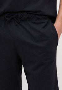 Schwarze Hose mit elastischem Bund und Kordelzug, aus weichem Baumwollmaterial gefertigt. Verfügt über seitliche Taschen und eine lockere Passform.