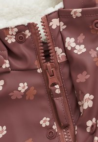 Vandskilt maroon jakke med blomstermønster, der har en blød hvid foring, en midterplaceret lynlås og trykknaplukninger.
