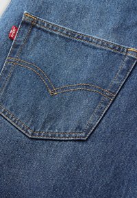 Blå denimficka med en böjd design, orange sömmar och en liten röd flik. Texturen är jämn med en något bleknad yta.