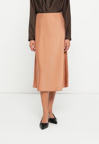 Midi-rok in glad, perzikkleurig stof met een lichte glans. Heeft een flatterende A-lijn snit en een tailleband, gecombineerd met puntige zwarte flats.