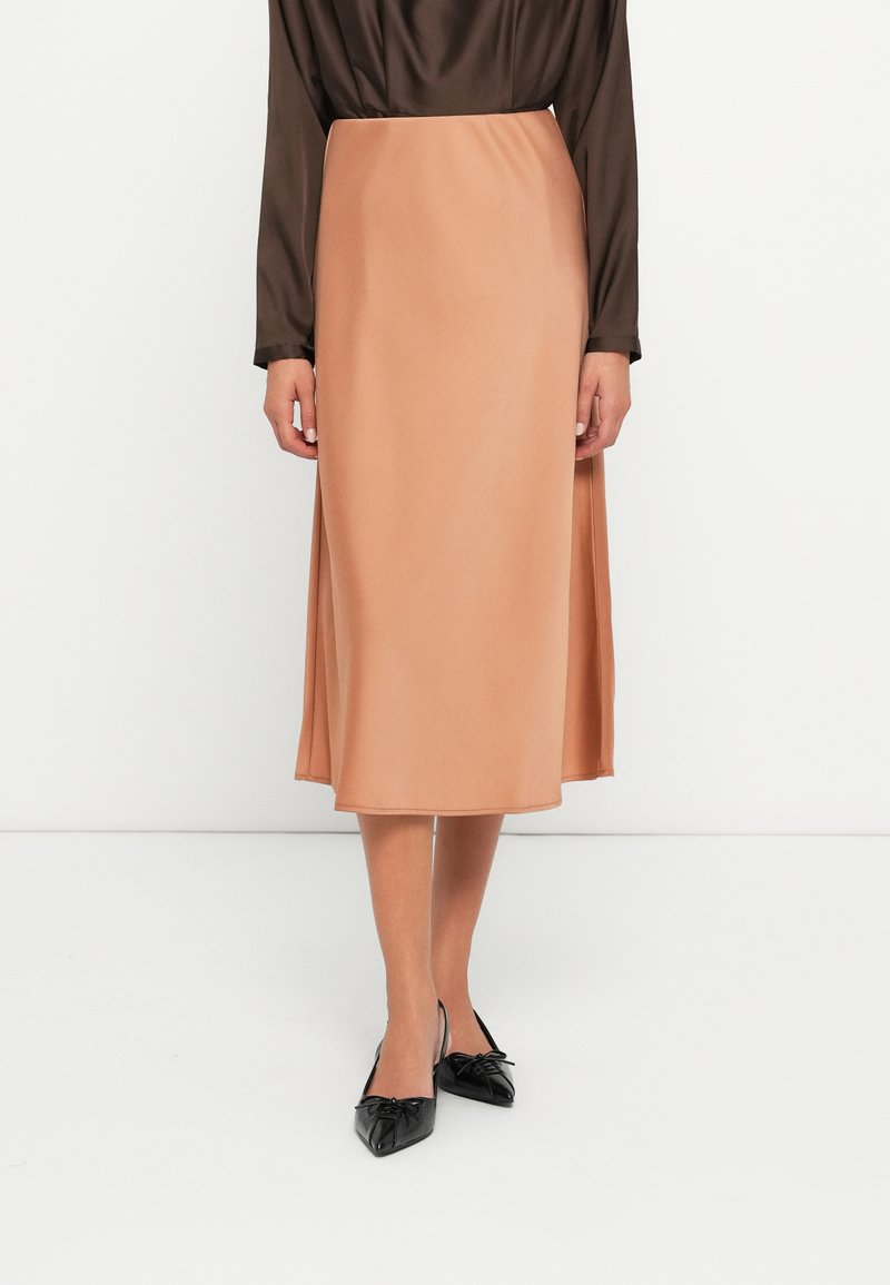 Midi-rok in glad, perzikkleurig stof met een lichte glans. Heeft een flatterende A-lijn snit en een tailleband, gecombineerd met puntige zwarte flats.