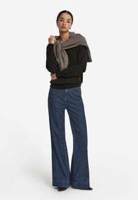 Schwarzer Pullover, lockere, dunkelblaue Denim-Hosen mit weitem Bein, grauer Schal über die Schultern drapiert, einfaches Design, glatte Textur, keine Muster.