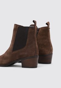 Brown suede ankle boots with a block heel, elastic side panels, and a zipper closure. Simple and sleek design with a textured finish.