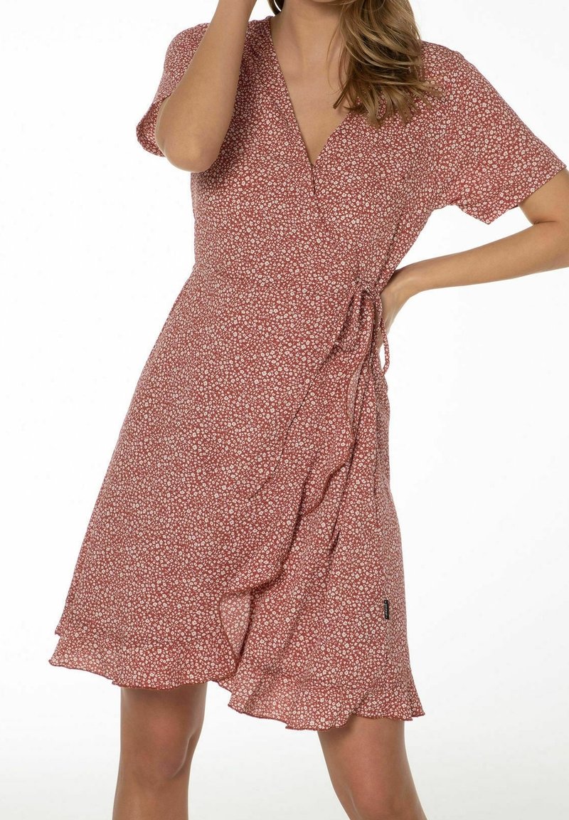 Röd blommig omslagsklänning med korta ärmar, V-ringning och en volang nederkant. Tyget har små vita blommor och en sidoknytdetalj.