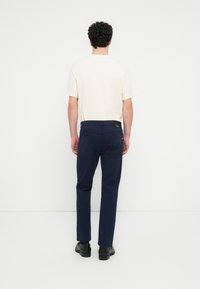 Pantalon bleu marine à coupe droite, en coton, avec une ceinture plate et des poches arrière. Porté avec un t-shirt crème clair.