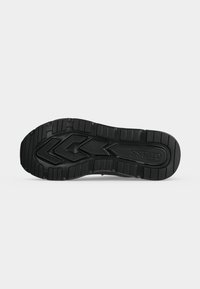 Semelle de chaussure en caoutchouc noir avec des rainures profondes, des motifs géométriques et le nom de la marque "GUESS" embossé près du talon.