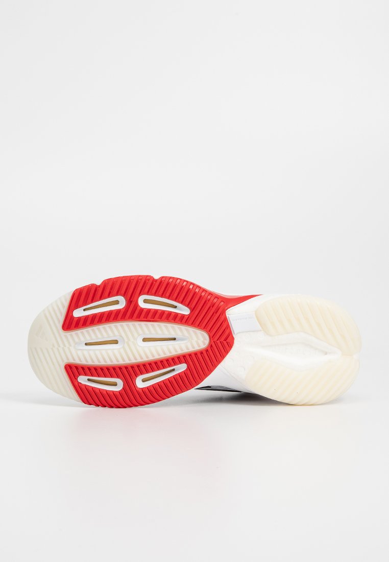 Suela de zapatilla blanca con una sección de goma roja texturizada y acentos transparentes. Surcos y recortes notables para tracción y flexibilidad.