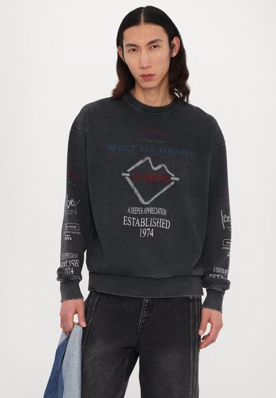 Sweatshirt gris foncé avec un col rond. Présente des textes et graphiques colorés imprimés sur le devant et les manches. Tissu en mélange de coton, coupe décontractée.