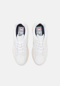 Baskets de sport blanches avec une tige en cuir lisse, des lacets plats, un col rembourré et une semelle en caoutchouc de couleur claire. Présente une marque sur la languette.