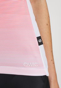 Gros plan d'un top sans manches rayé rouge et blanc avec une étiquette de logo noire et un texte blanc "OWIC" près de l'ourlet, porté avec un bas noir.