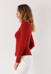 Maglietta rossa a maniche lunghe con design aderente, morbida al tatto e con scollatura rotonda, abbinata a pantaloni bianchi slim-fit.