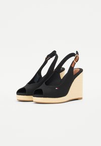 Sandali wedge neri in tela con punta aperta, cinturino alla caviglia e una piattaforma in juta texturizzata. Presentano un piccolo dettaglio del logo sul lato.