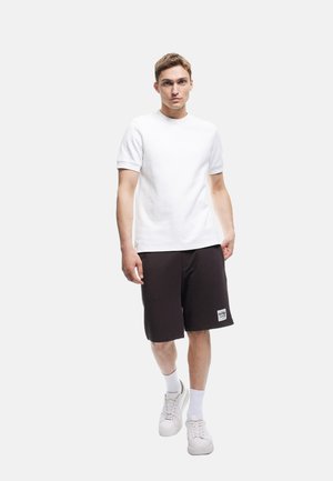 Witte korte mouwen t-shirt gecombineerd met zwarte shorts, met een eenvoudig ontwerp. Model draagt witte sneakers en geribde enkelsokken.