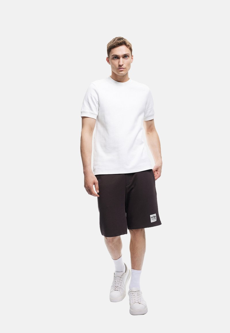 Witte korte mouwen t-shirt gecombineerd met zwarte shorts, met een eenvoudig ontwerp. Model draagt witte sneakers en geribde enkelsokken.