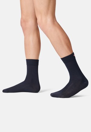 Marineblaue Socken mit einem gerippten Bündchen und glatter Textur, die dezente Musterdetails und ein kleines Logo-Element aufweisen.