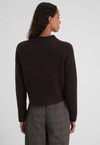 Pull court marron en maille douce, avec un col et un ourlet côtelés. Porté avec un pantalon gris à carreaux, affichant une coupe décontractée.