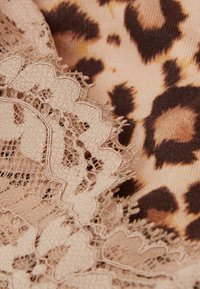 Tela de estampado de leopardo en tonos de beige y marrón, acentuada con un delicado borde de encaje de un suave beige, con bordes ondulados.
