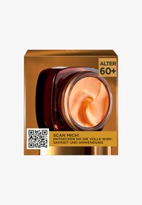 Röd burk med en virvlande, persikofärgad kräm inuti. Asken har guldfärgade detaljer och en QR-kod, märkt för användare som är 60 år eller äldre.