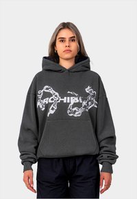 Haut à capuche oversize gris foncé avec une poche frontale, arborant un motif de chaîne blanche et un logo. Tissu texturé avec des poignets et un ourlet côtelés.
