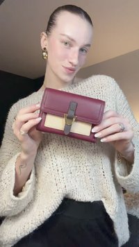 Tumši sarkanas ādas maks ar bēša krāsas paneli un teksturētu tumši brūnu siksniņu. Aprīkots ar zelta toņa aizdari un kompakta taisnstūra dizainu.